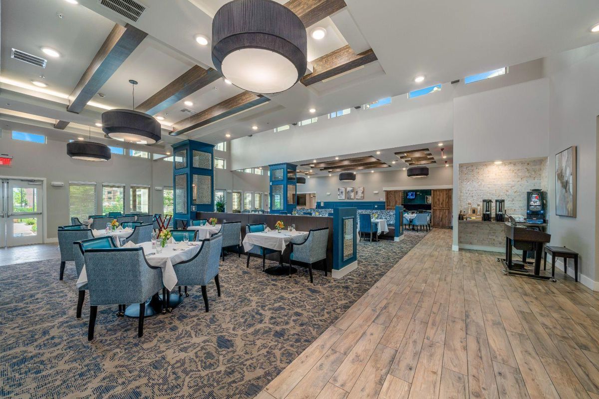 A modern restaurant interior with elegant chandeliers, carpeted floors, and neatly arranged tables and chairs.