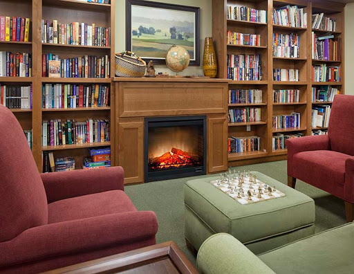 A cozy library setting with comfortable seating, a fireplace, and shelves filled with books.