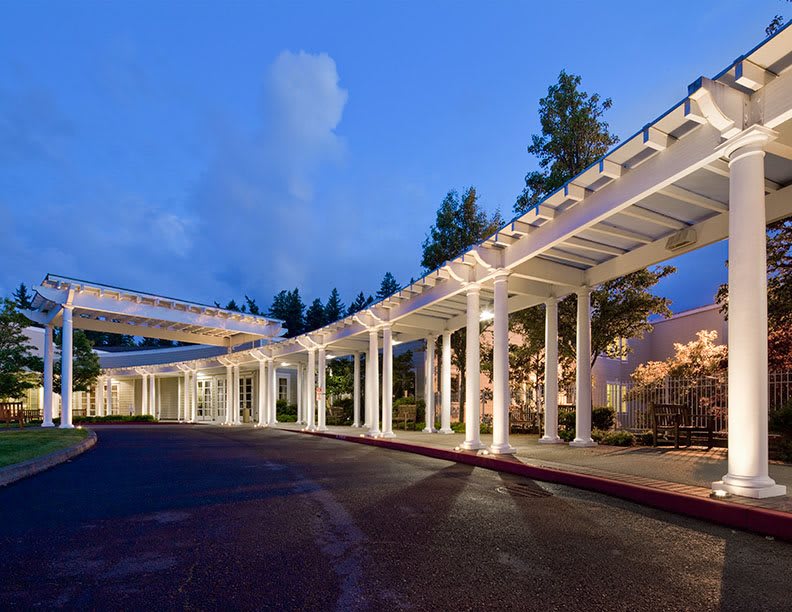 A modern hospital building with a covered walkway, illuminated at night.