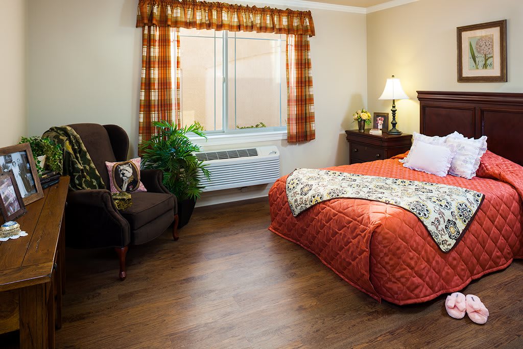 A cozy bedroom with a bed, armchair, and window adorned with curtains.