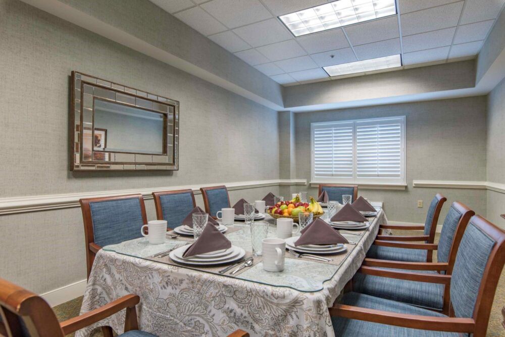 A formal dining room setup with a table elegantly arranged with plates, napkins, and glasses, surrounded by upholstered chairs.