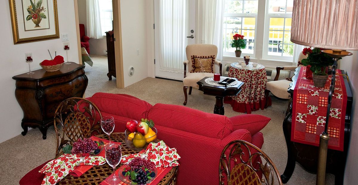 A cozy living room with a red couch and dining area, complemented by vibrant decor and natural light from the windows.