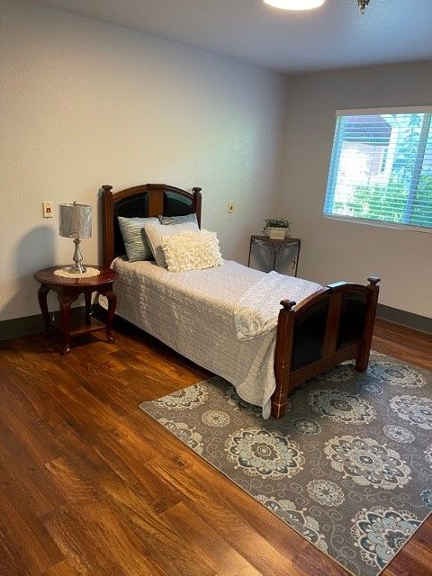 A neatly arranged bedroom with a single bed, nightstand, and a lamp on a wooden floor.