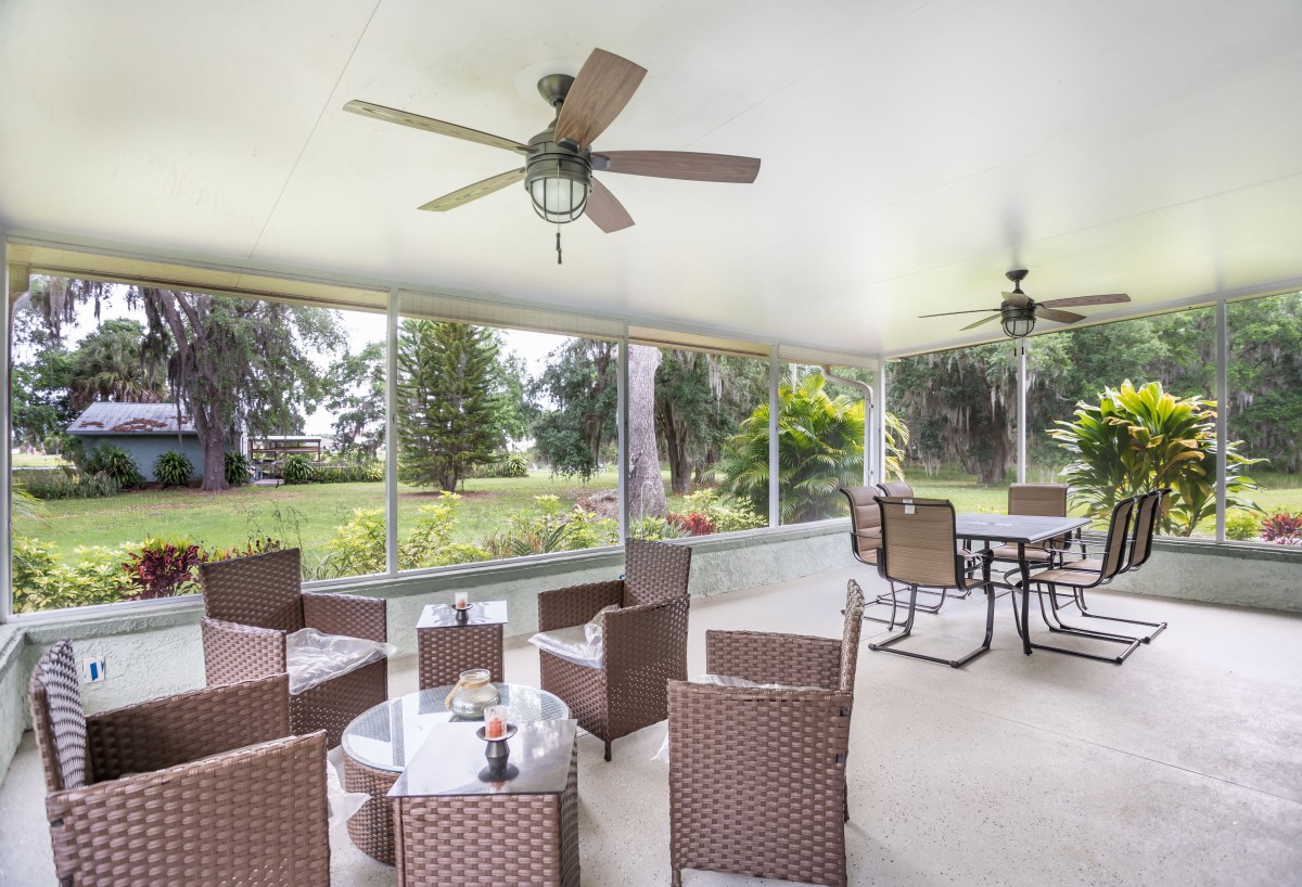 A cozy patio with comfortable seating and ceiling fans, overlooking a lush garden.