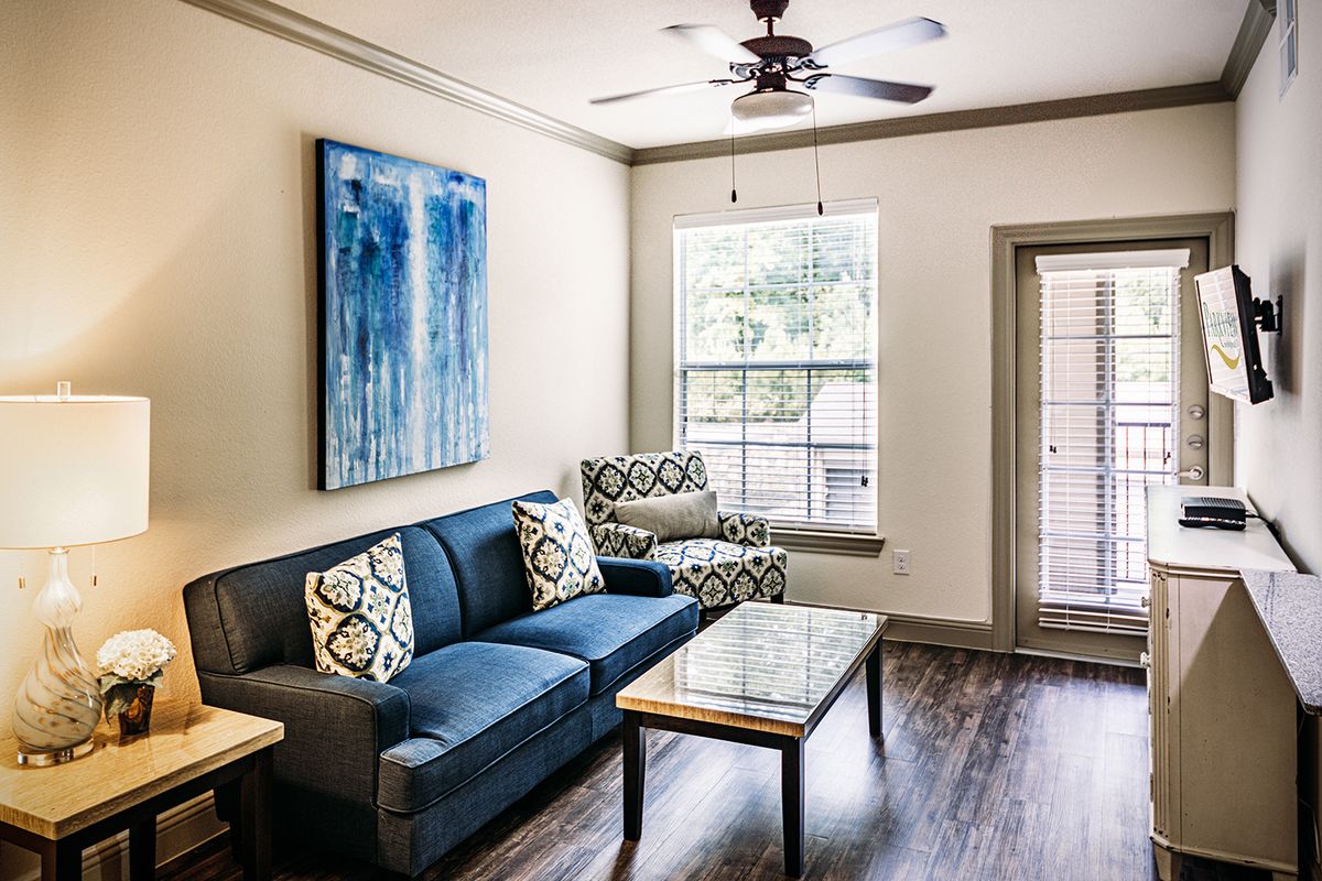 A modern living room featuring a blue sofa, patterned armchair, and a coffee table under a ceiling fan.