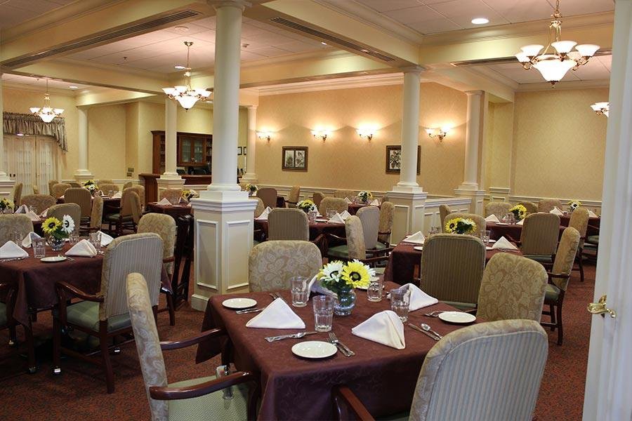 An elegantly set dining area with neatly arranged tables and chairs, adorned with floral centerpieces.