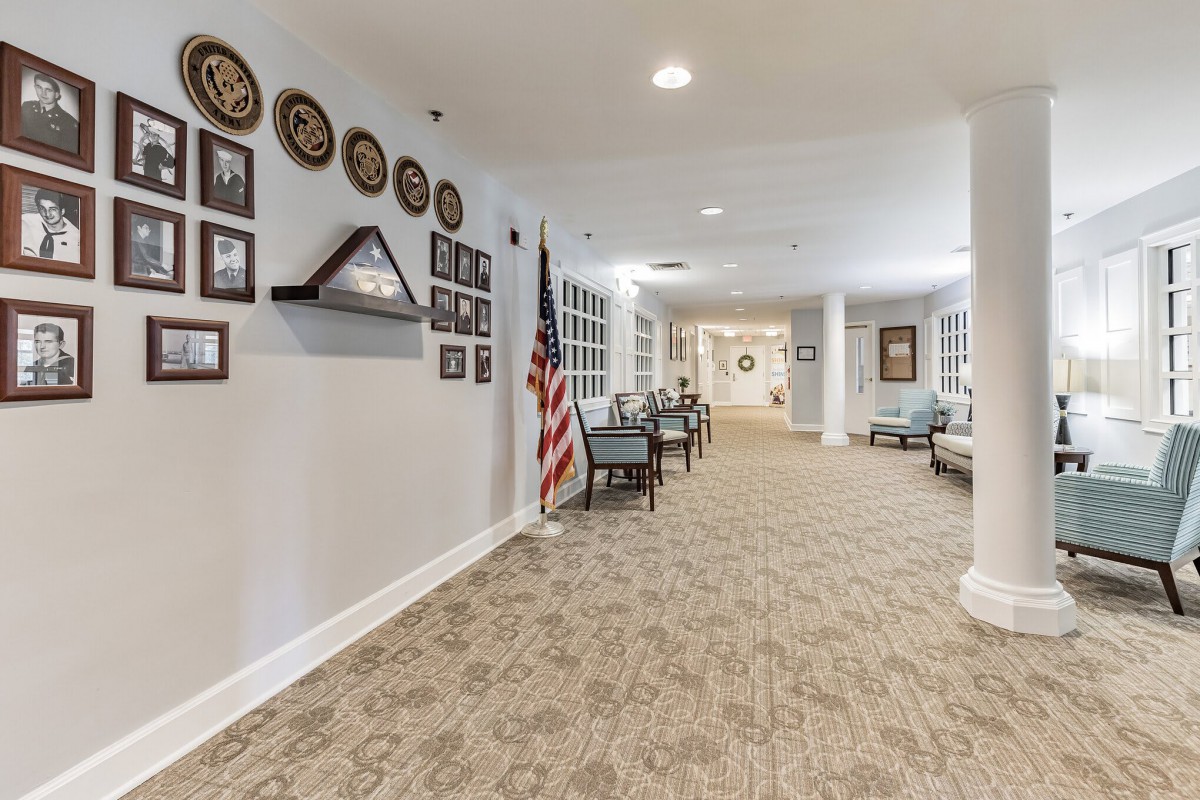 A long hallway with wall decorations, an American flag, and rows of chairs along the carpeted floor.