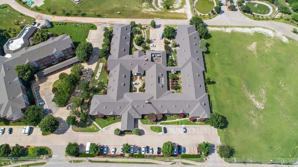 An aerial view of a large building complex with surrounding greenery and a parking lot.