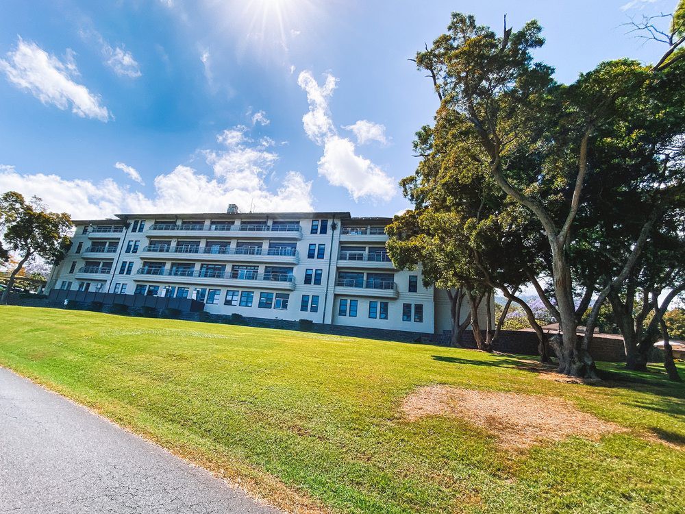 A residential building surrounded by grass and trees under a partly cloudy sky.