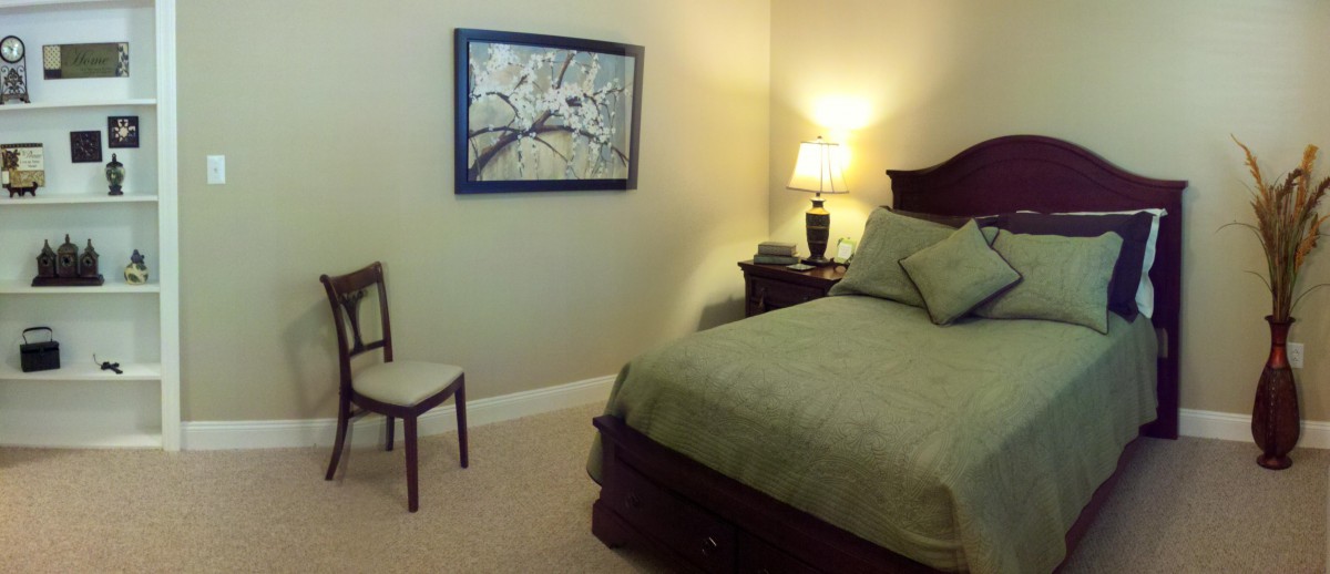 A cozy bedroom with a neatly made bed, a lamp on the nightstand, and artwork hanging on the wall.