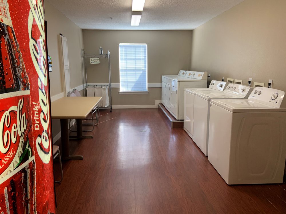A clean and organized laundry room with several washing machines, dryers, a vending machine, and a table.