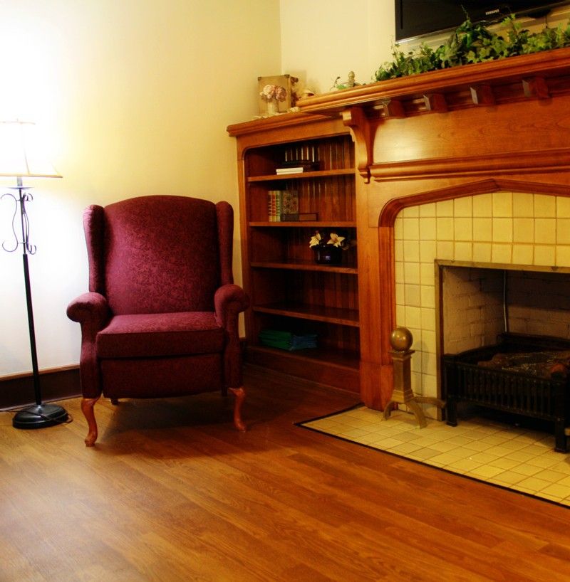 A cozy living room with an armchair, bookshelf, and a fireplace.
