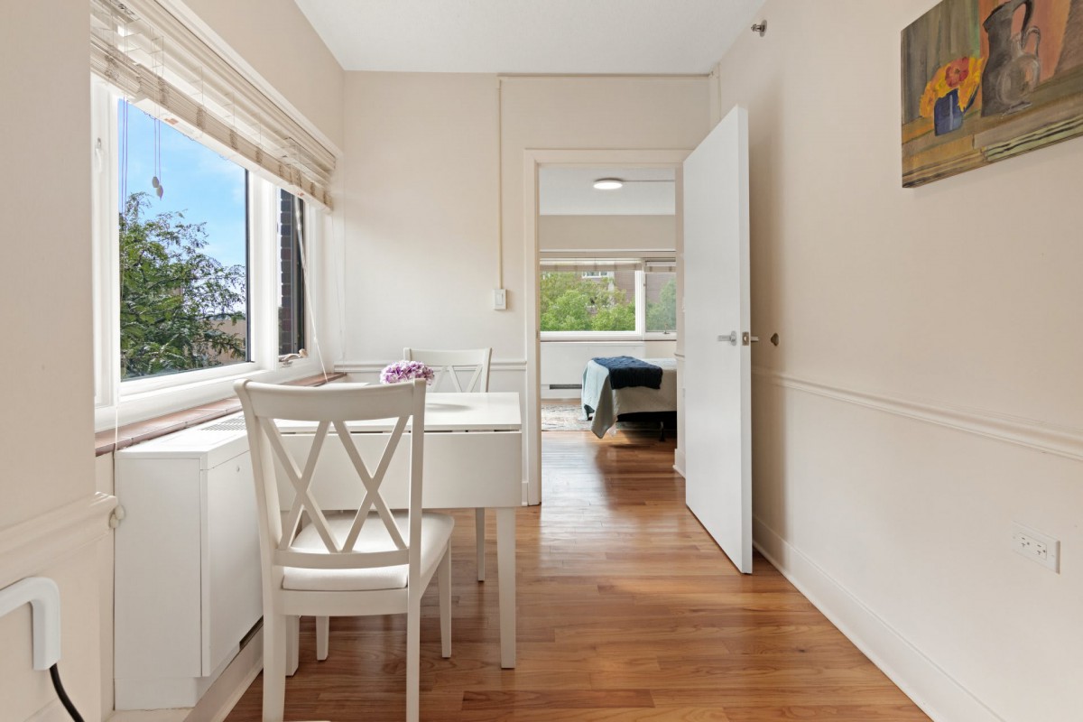 A bright bedroom with a desk and chair by the window, featuring hardwood flooring.