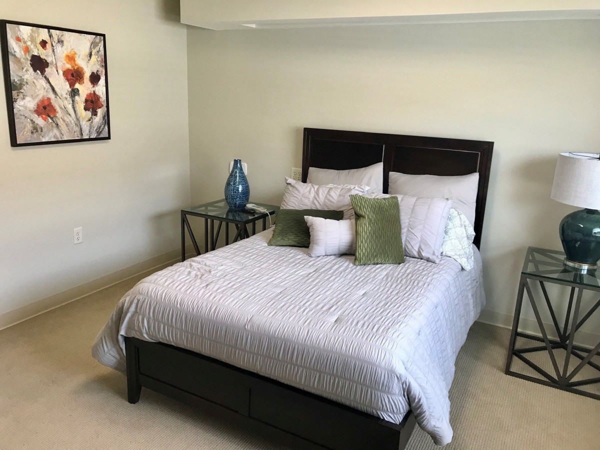 A neatly arranged bedroom with a comfortable bed, decorative pillows, nightstands, and a piece of wall art.