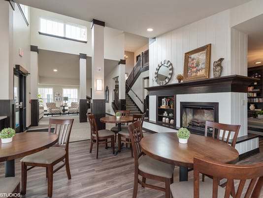 A modern living and dining area featuring a fireplace, wood flooring, and an elegant staircase.