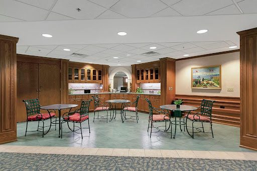A cozy cafeteria setting featuring round tables and chairs, with wooden cabinetry and soft lighting.