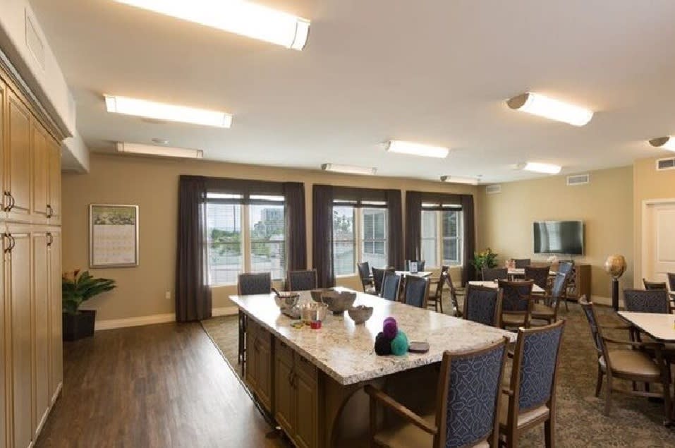 A spacious dining room with large tables and chairs, illuminated by overhead lights and natural light from expansive windows.