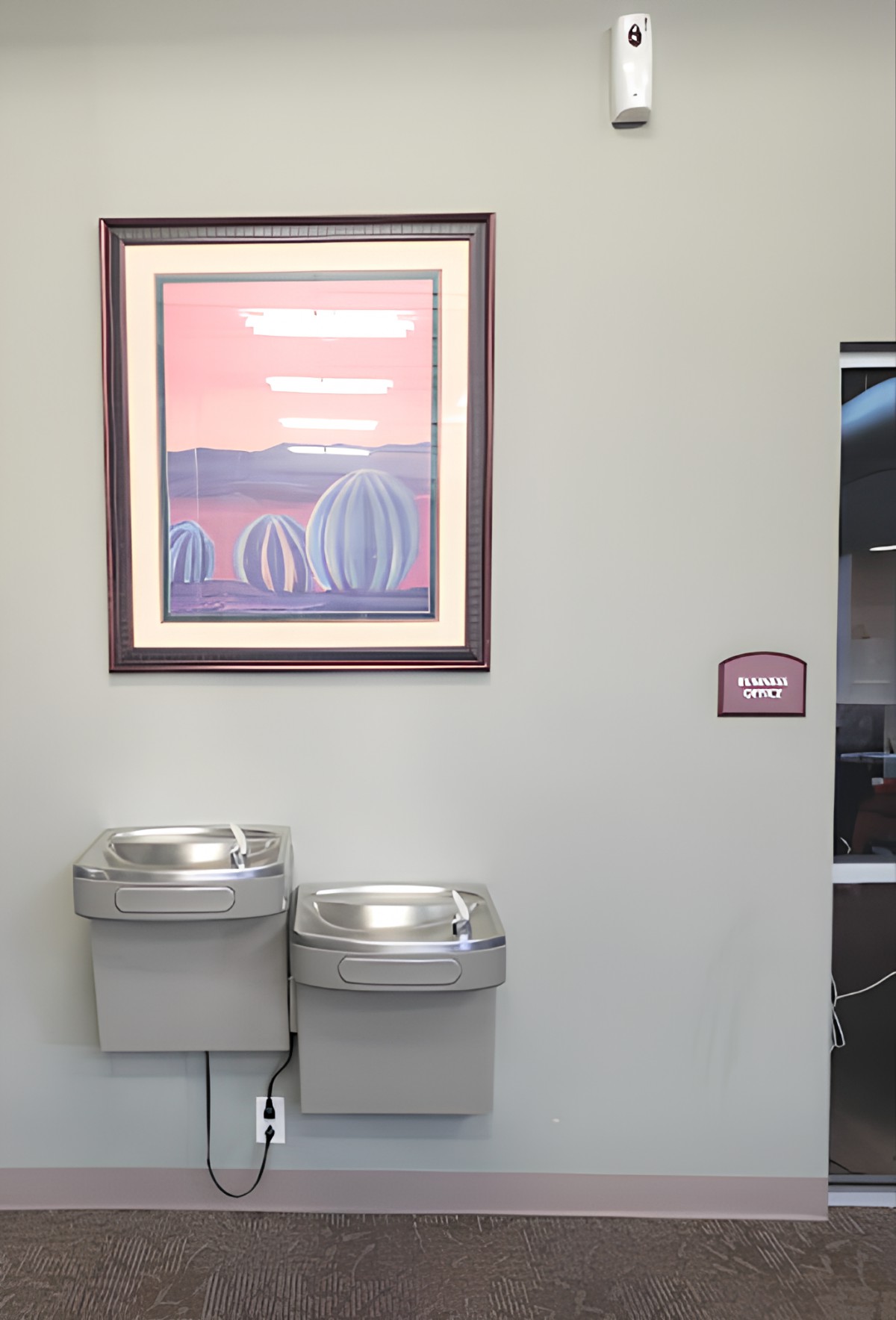 A public area with two water fountains and a framed painting on the wall.