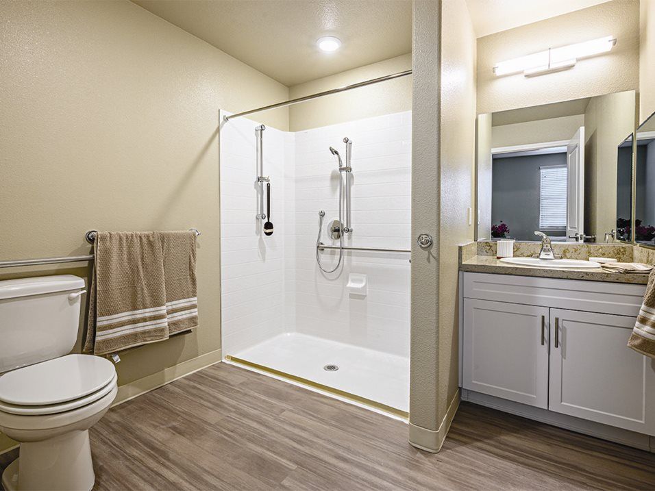 A modern bathroom featuring a spacious shower, toilet, sink with mirror, and neatly arranged towels.