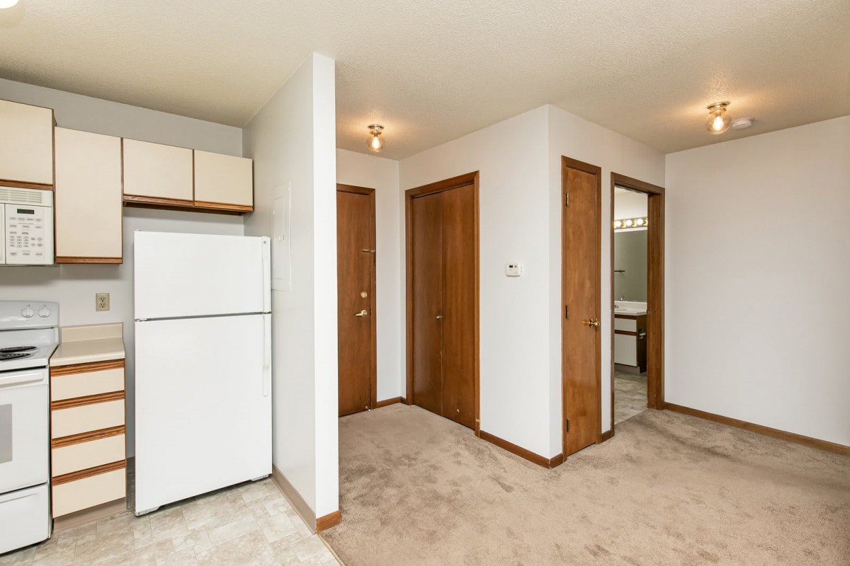 A small apartment interior featuring a kitchen area with a fridge and wooden doors leading to other rooms.