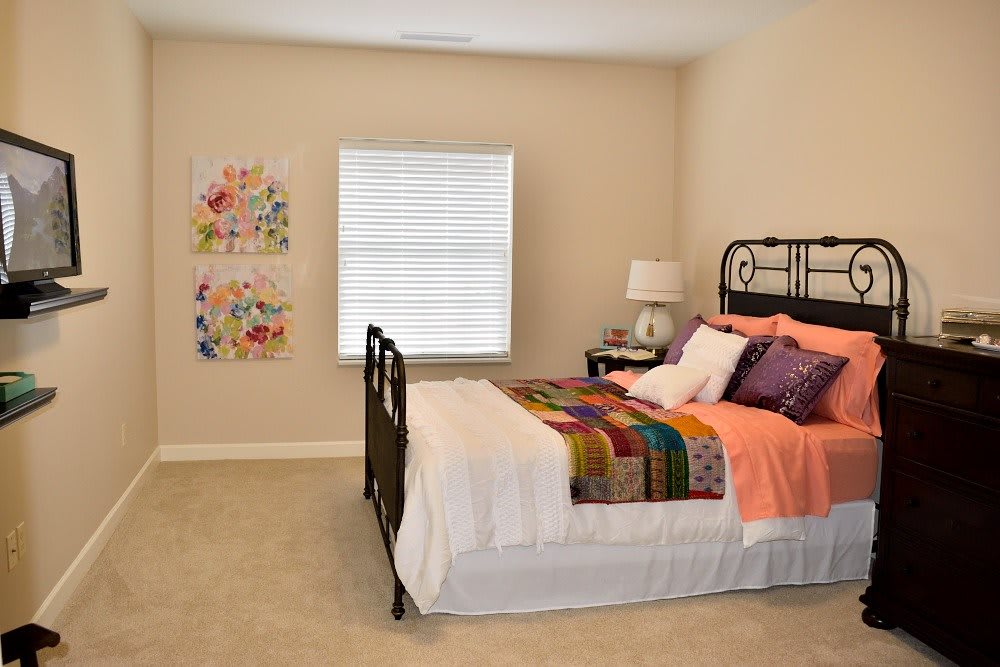 A cozy bedroom with colorful bedding and wall art, featuring a window and bedside lamp.