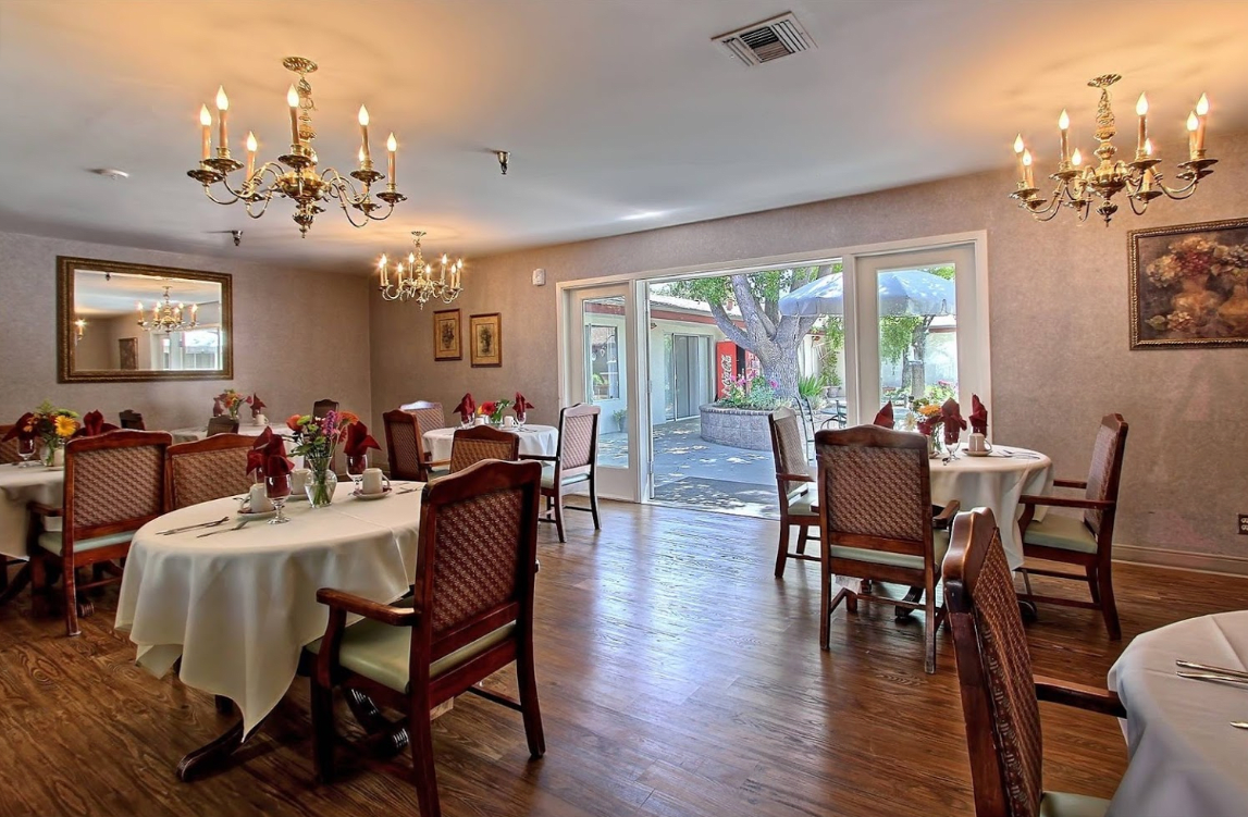 An elegant dining room with chandeliers, set with tables and chairs on a wooden floor.