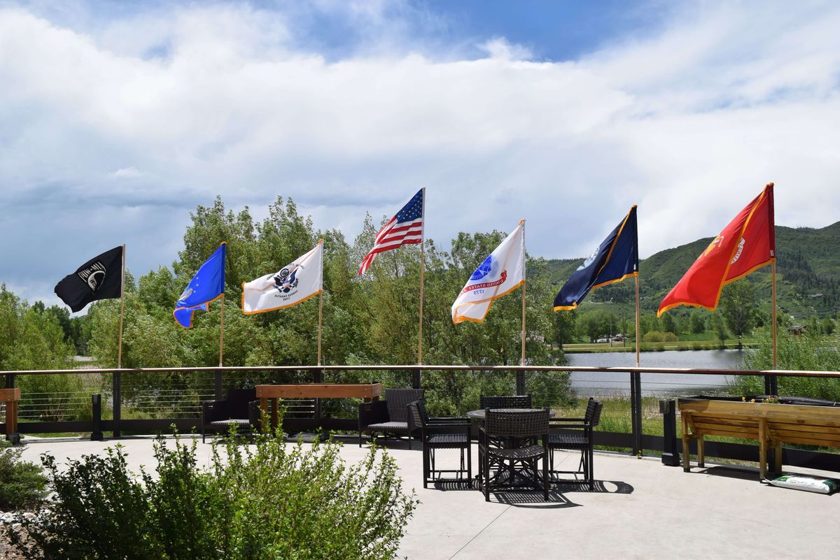 A patio with outdoor seating and a row of flags against a scenic backdrop of trees and hills.