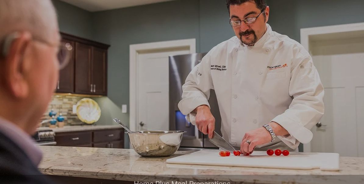 A chef in a professional kitchen chopping ingredients on a cutting board.
