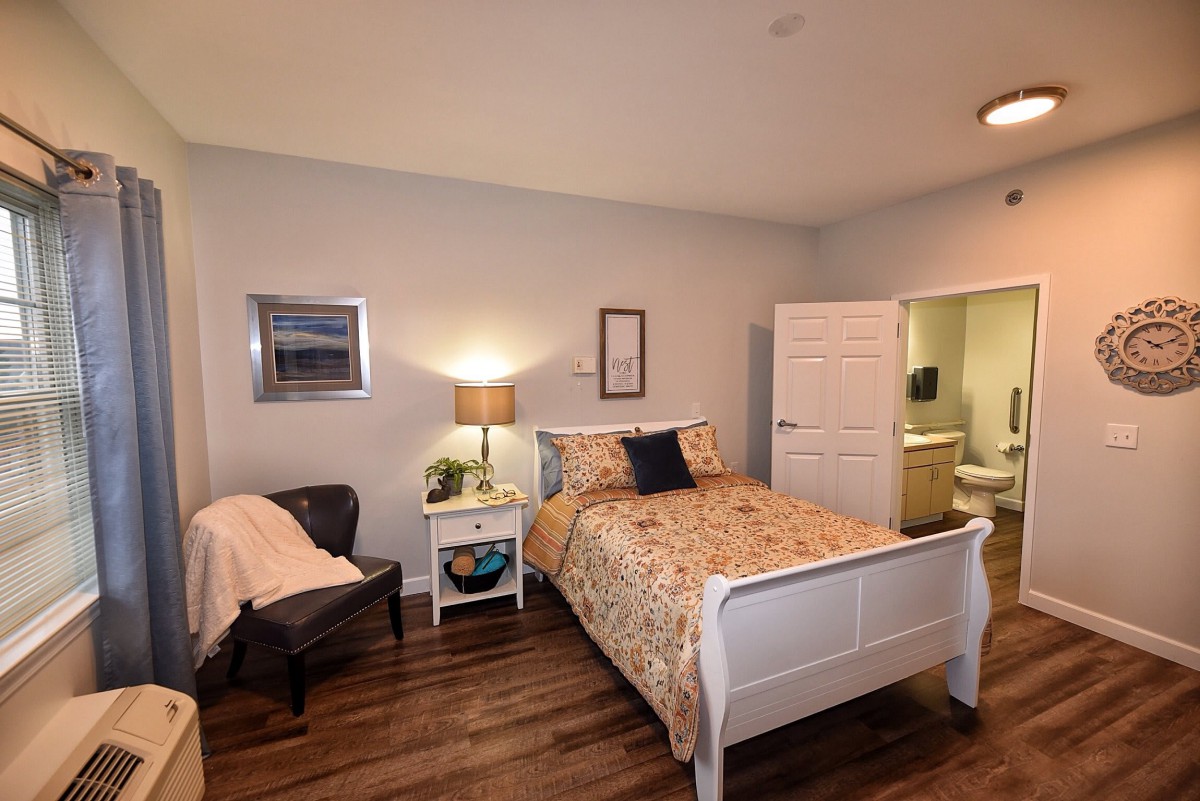 A cozy bedroom with a bed, lamp, chair, and wooden flooring.