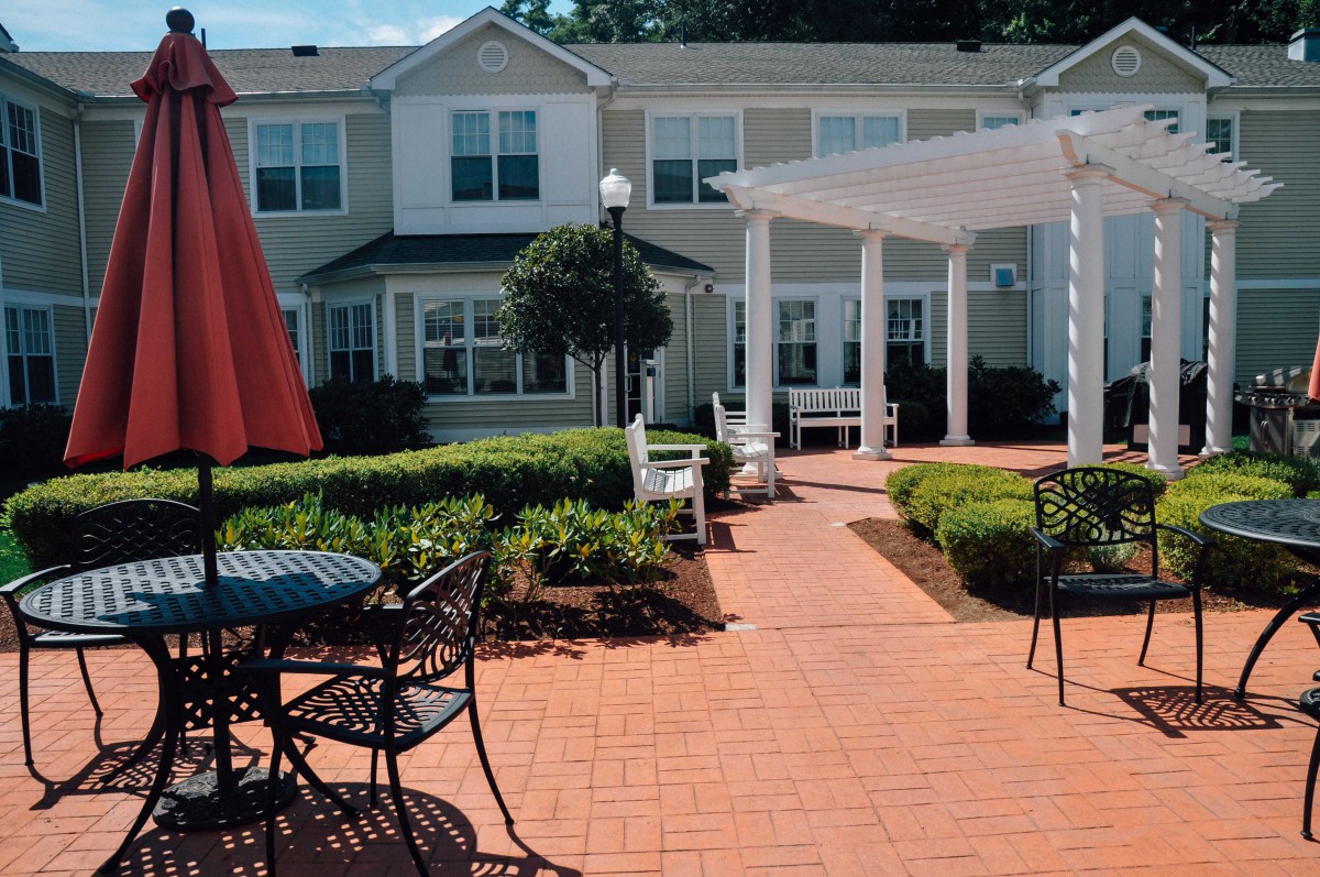 A sunny courtyard features outdoor seating and a pergola, surrounded by a well-maintained garden.