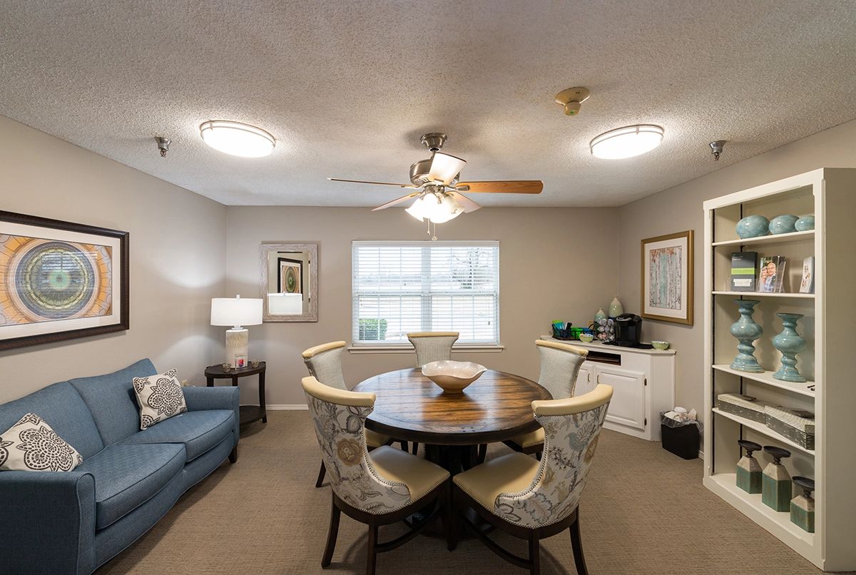 A cozy living and dining area with a wooden table, comfortable chairs, and a sofa under soft lighting.