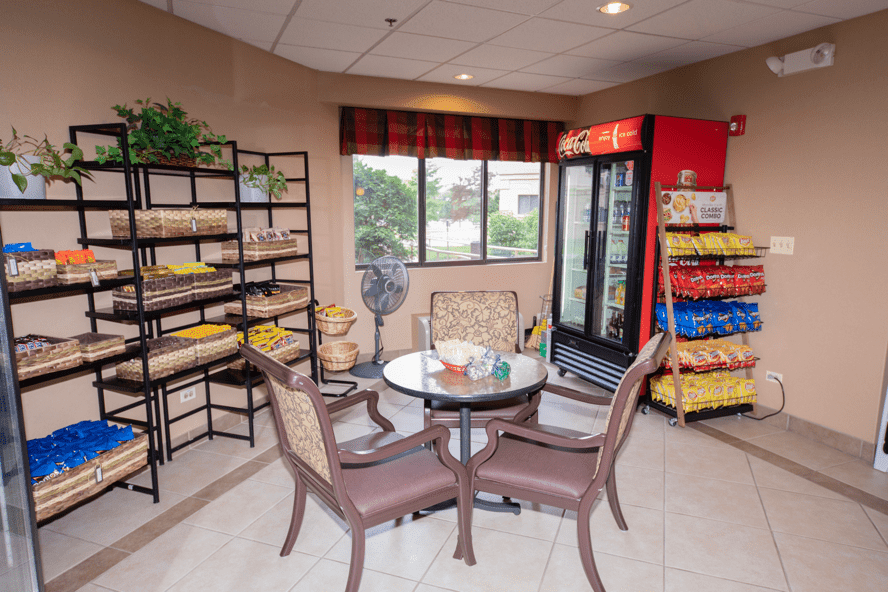 A snack area with tables and chairs, featuring shelves stocked with snacks and a refrigerator.