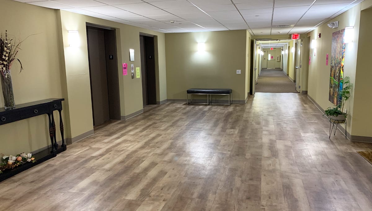 A hotel hallway with elevators and a bench on a wooden floor.