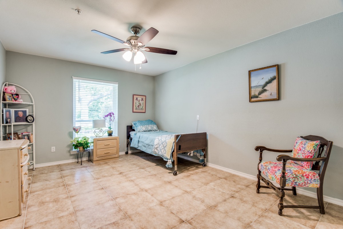 A simple bedroom with a single bed, ceiling fan, and tiled floor.