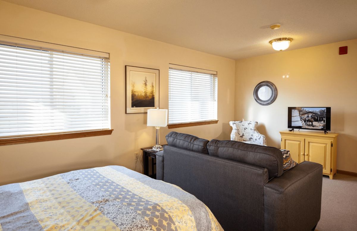 A cozy bedroom featuring modern decor with a bed, couch, and bedside lamp.