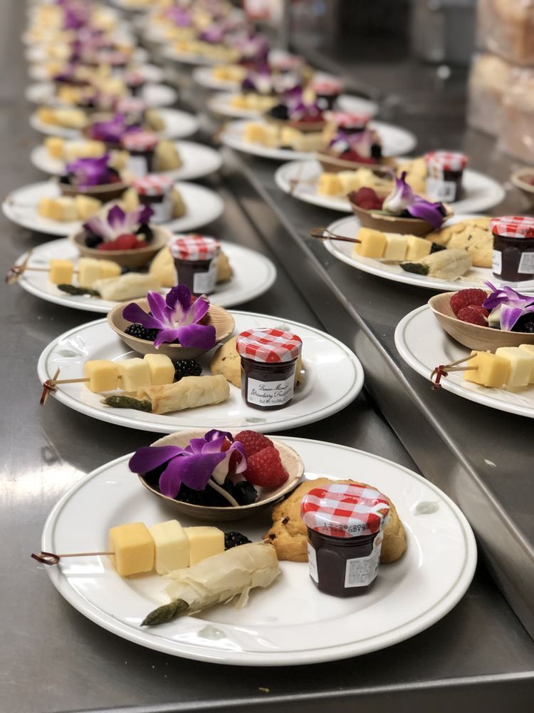 A selection of elegantly plated appetizers featuring cheese cubes, jam jars, and fruit skewers.