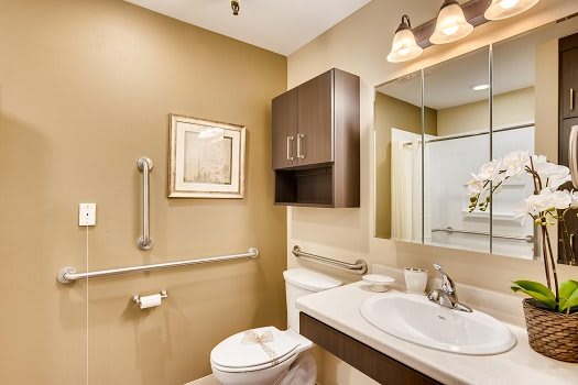 A well-lit, modern bathroom with a toilet, sink, mirror, and storage cabinet.