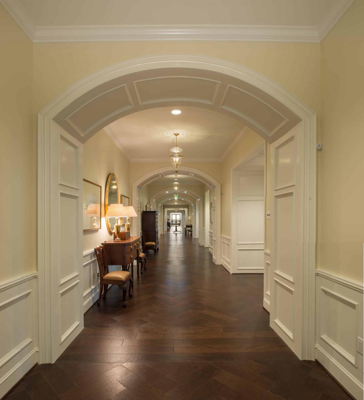 A long hallway with wooden floors and classic arch design, featuring elegant furniture and soft lighting.