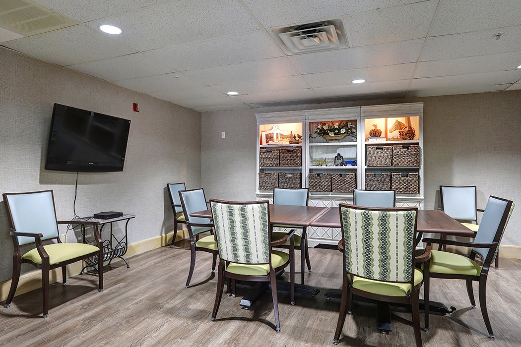 A modern meeting room with tables, chairs, a television, and shelves.