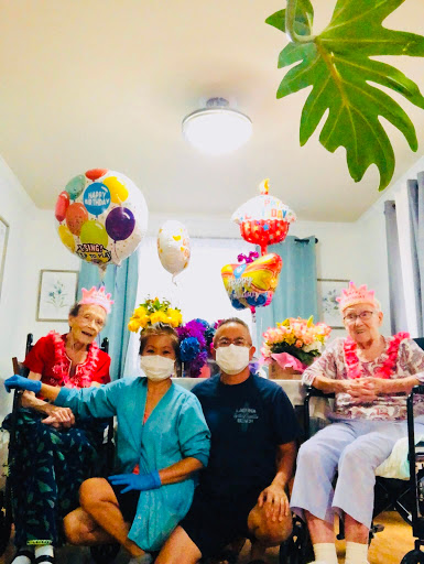 A joyful celebration with senior residents and caregivers surrounded by colorful balloons and vibrant decorations.