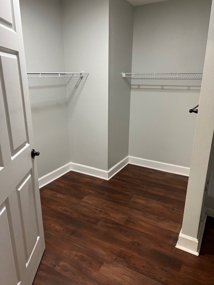An empty walk-in closet with wooden flooring and white shelving.