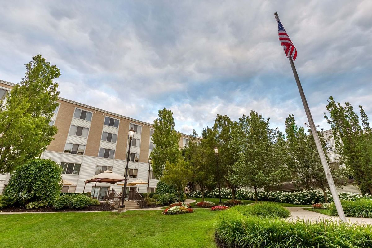 A well-maintained outdoor area with a building, a flagpole, and lush greenery under a cloudy sky.