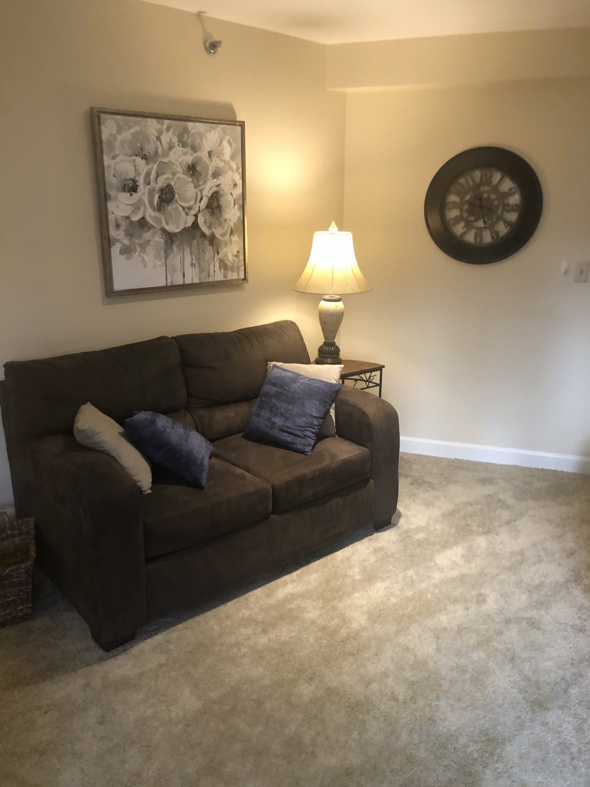 A cozy living room with a sofa, lamp, wall art, and a clock.