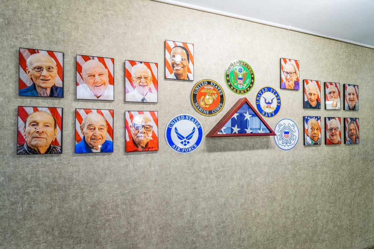 A wall display featuring portraits of veterans, military insignia, and a folded American flag.