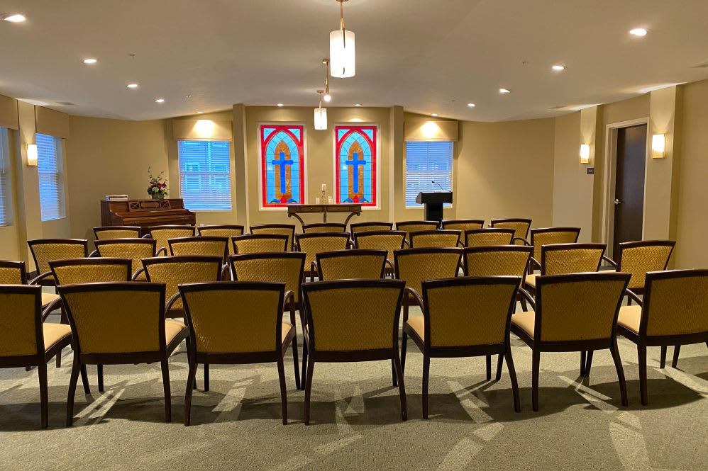 An interior view of a chapel with rows of chairs facing a pulpit and stained glass windows.