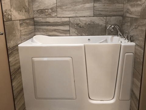 A bathroom featuring a walk-in bathtub with tiled walls.