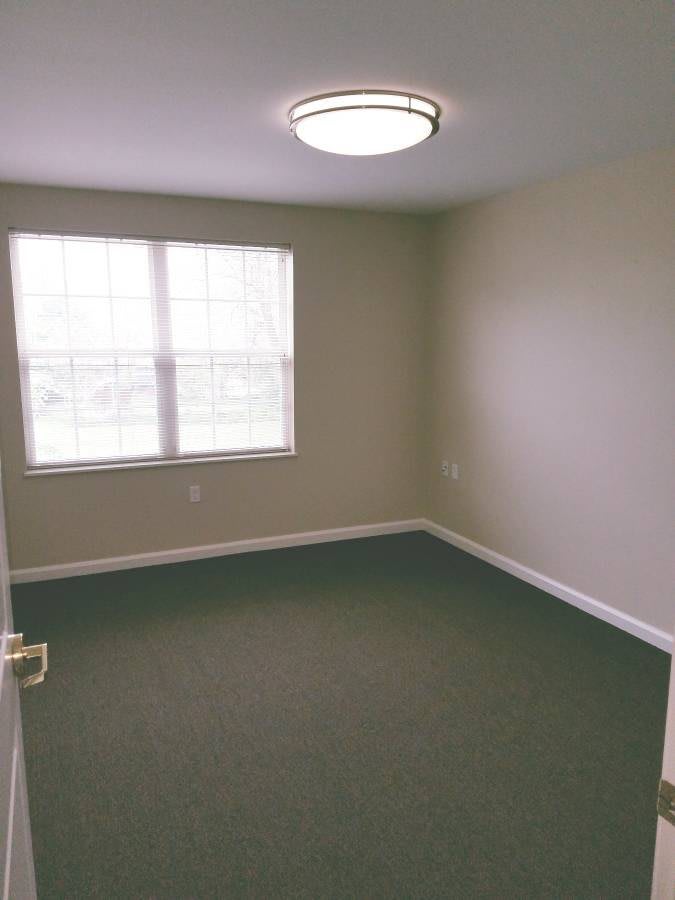 A simple, unfurnished room with a window and carpeted floor.