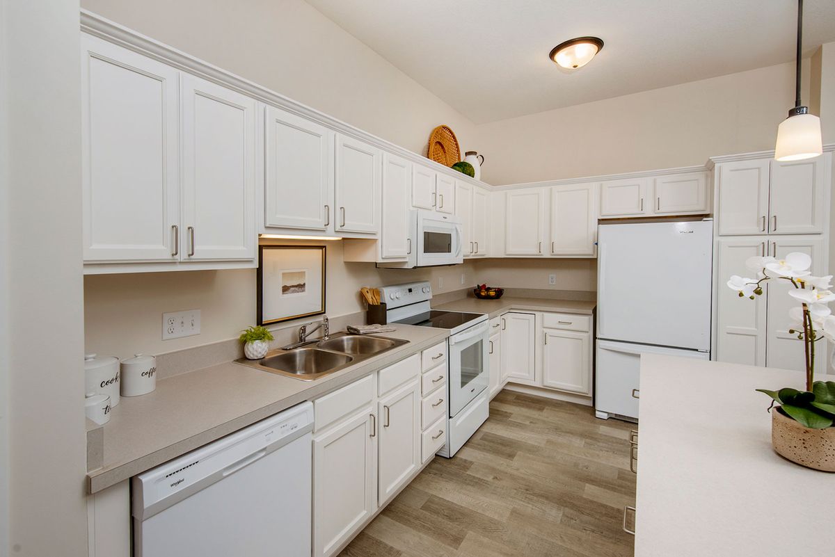 A modern kitchen with white cabinets and countertops, featuring a refrigerator, stove, microwave, and sink.