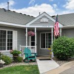 A cozy house with a small porch adorned by an American flag and surrounded by a well-maintained garden.