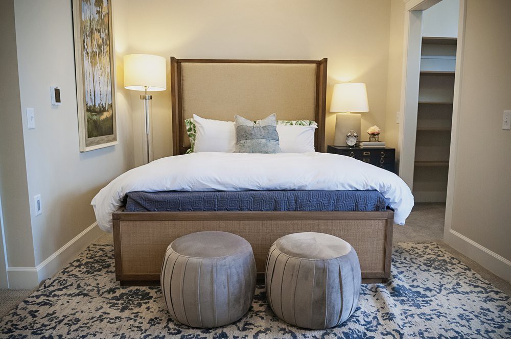A cozy bedroom with a large bed, two ottomans at the foot, and stylish lighting.